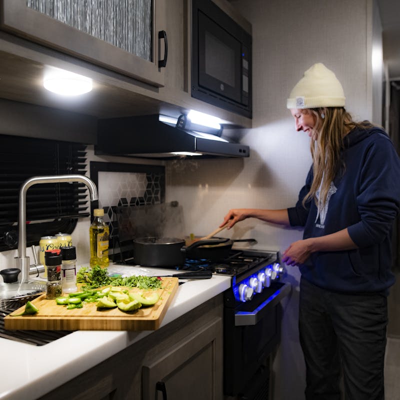 A woman cooks over the stove inside of an RV kitchen.