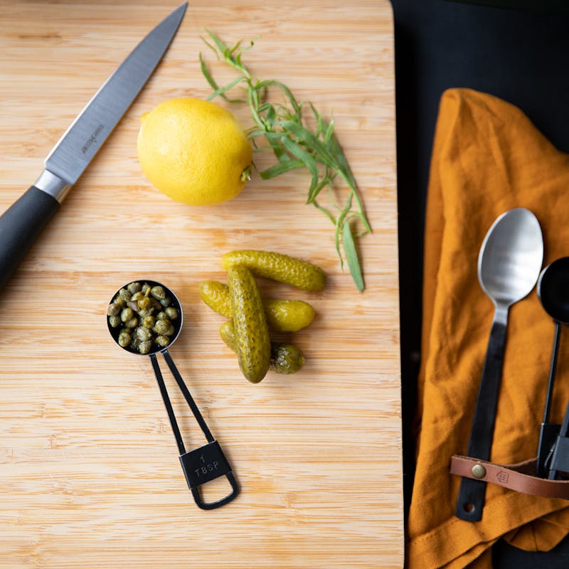 Gherkins, capers, lemon and thyme on a cutting board.