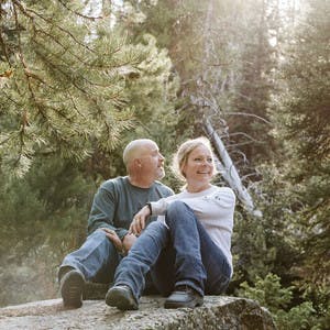 Steve & Suzanne Talbot sitting next to each other in a forrest smiling and enjoying each others company.