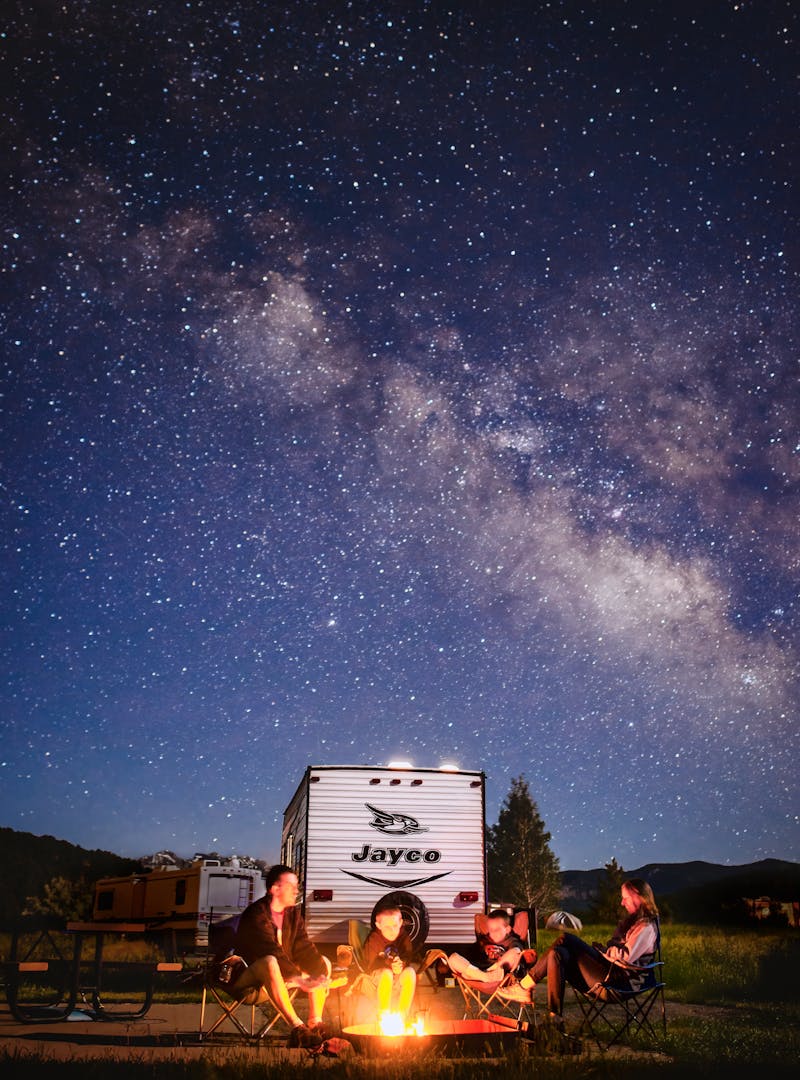 Alison Takacs's family around a campfire with their Jayco travel trailer and a starry sky in the background.