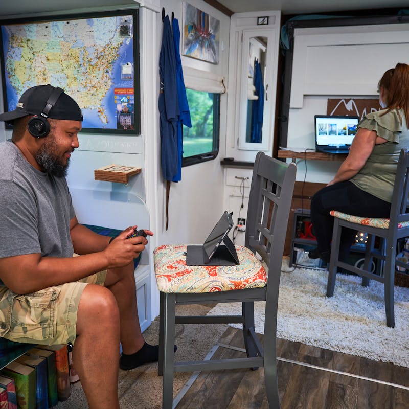 Christina McMillan working on the computer and Ben McMillan playing a video game inside their RV