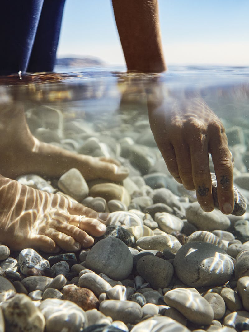 A woman picks up a rock from a shallow lake. 