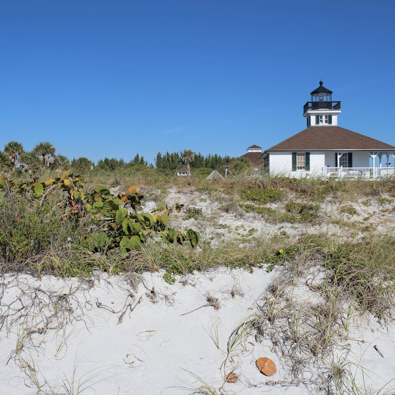 The Port Boca Grande Lighthouse on Gasparilla Island, Florida viewed from the sand dunes with sea oats and sea grape in the foreground and a clear blue sky