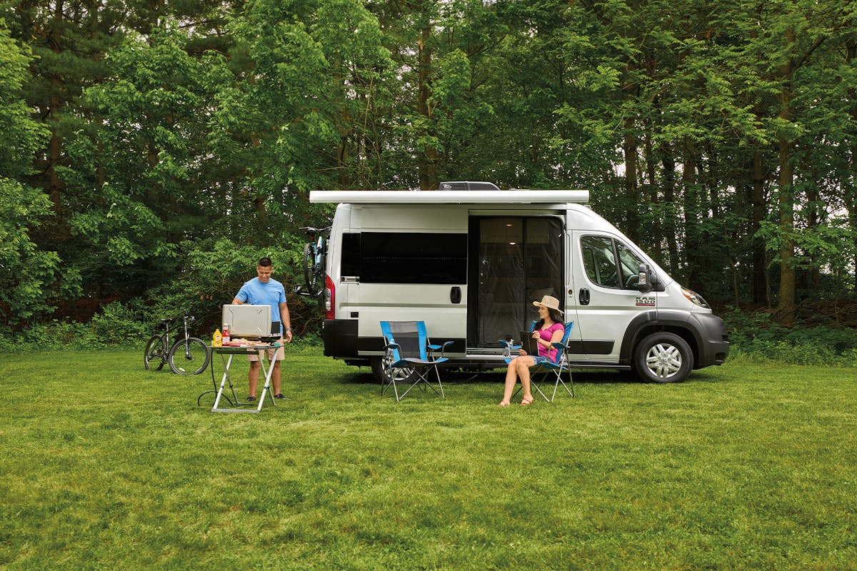 Thor Rize Class B Camper Van with family grilling outside surrounded by trees