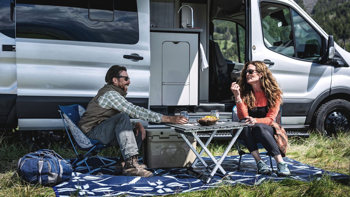 Couple enjoying a picnic outside of their Class B Motorhome on a sunny day