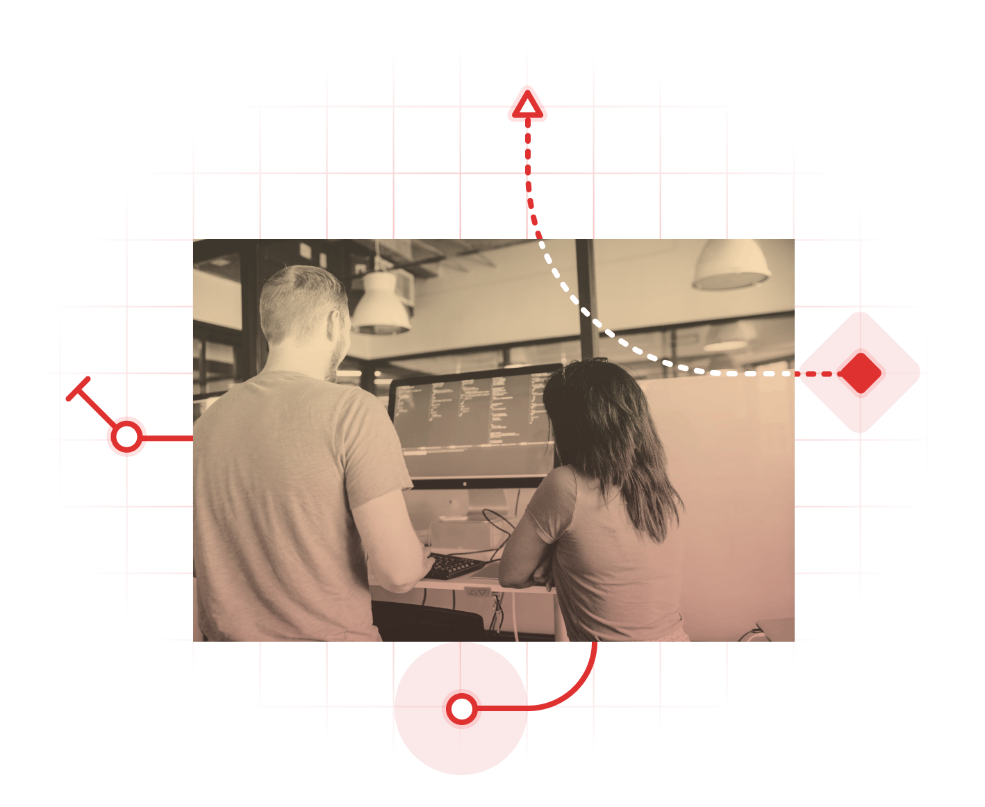 Two people standing around a desk, looking at a computer and collaborating.