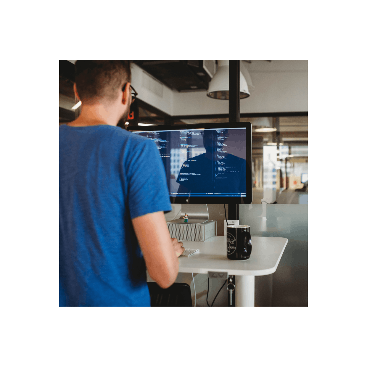 Person standing at a desk looking at a computer screen with code on it.