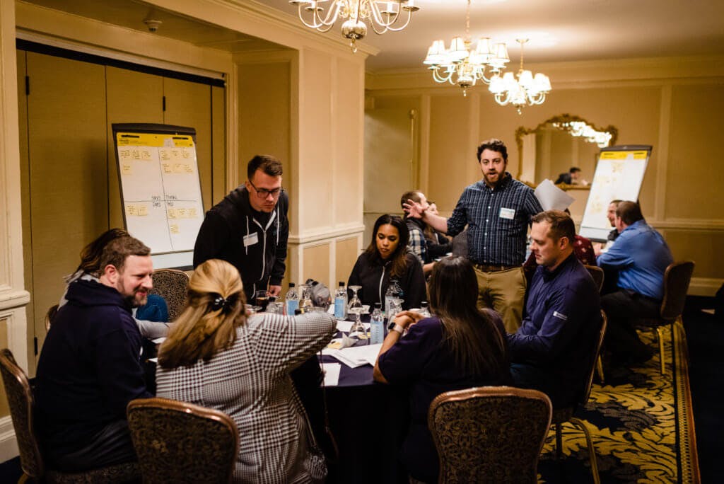 A thoughtbot facilitator standing around a table of Corvous employees and customers talking