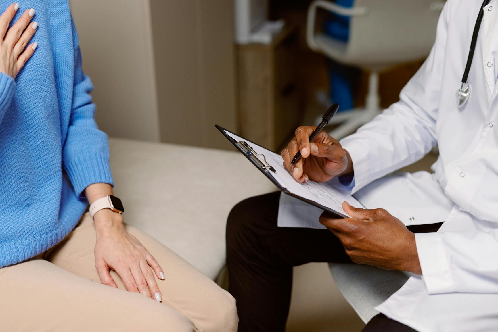 A patient and doctor with clipboard sit closely in a doctor's office