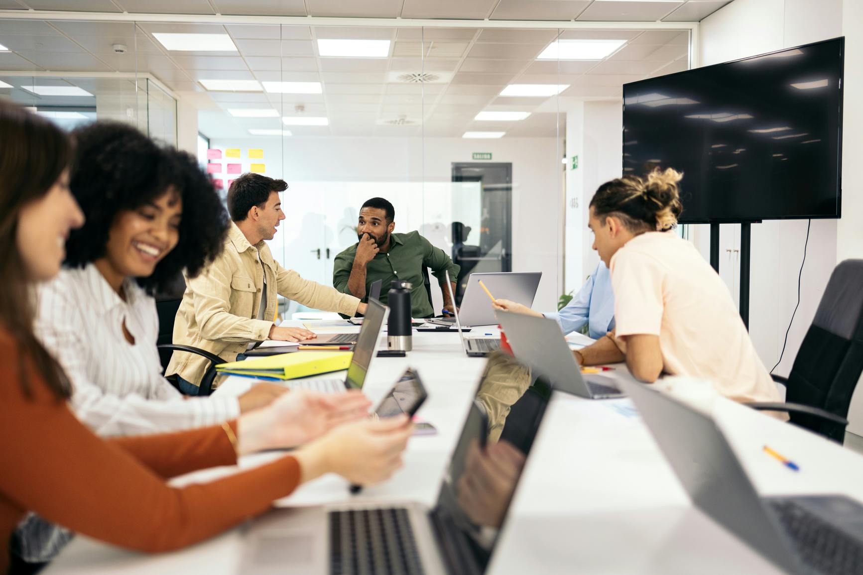 A group of diverse people talk and smile around computers on a conference table