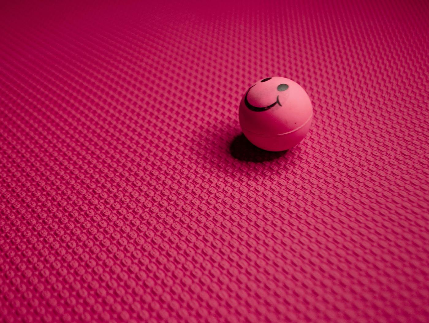 A pink bouncy ball with a smile sitting on a pink background
