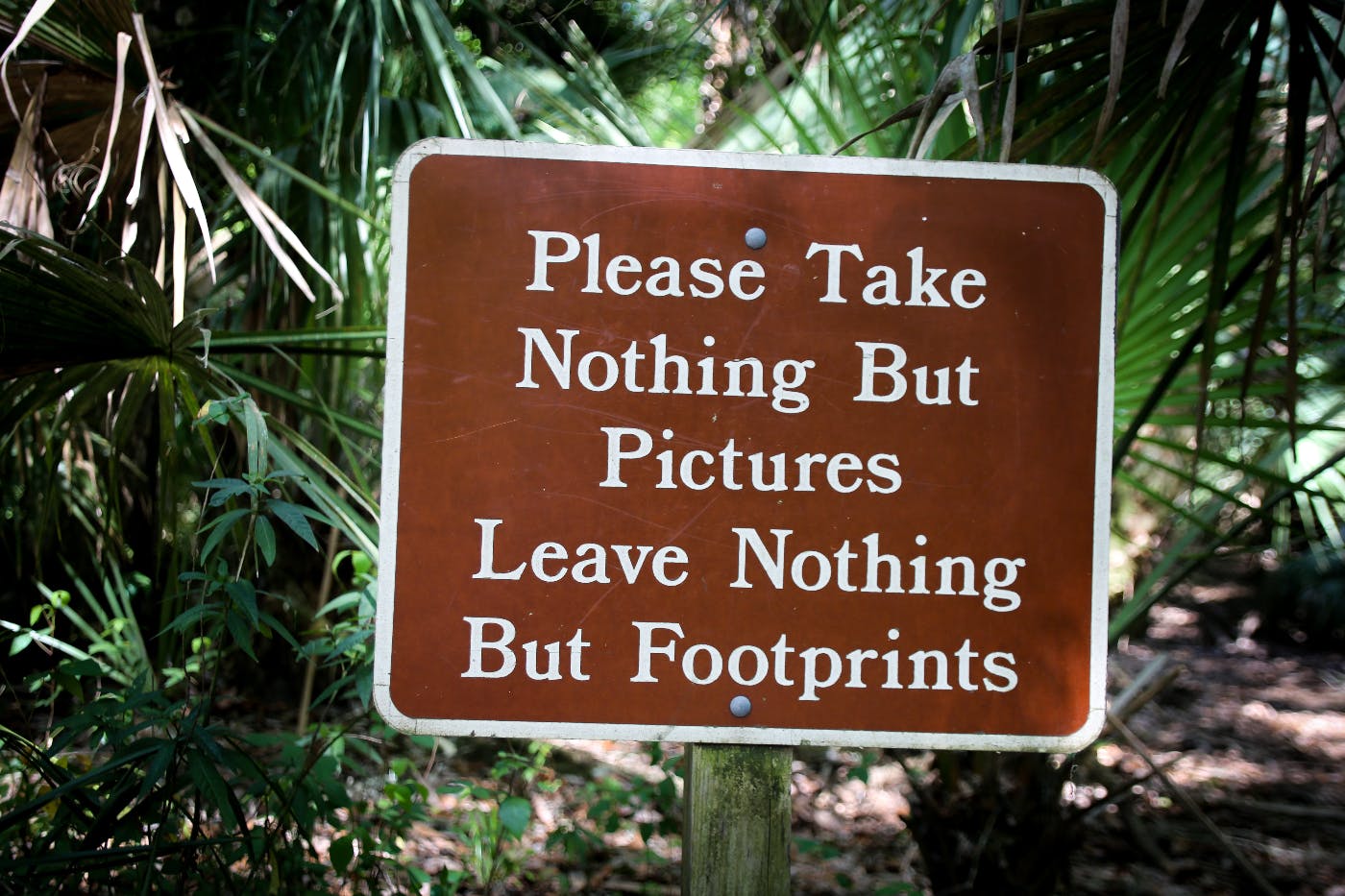 A national Park Sign reading "Please Take Nothing but Pictures Leave Nothing But Footprints."