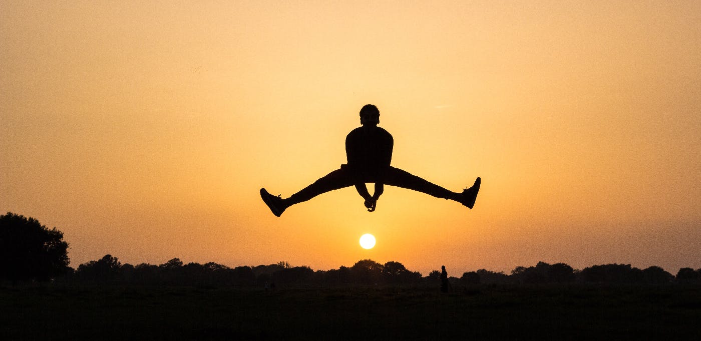 a man in silhouette doing a split in the air, looking like he's jumping over the setting sun