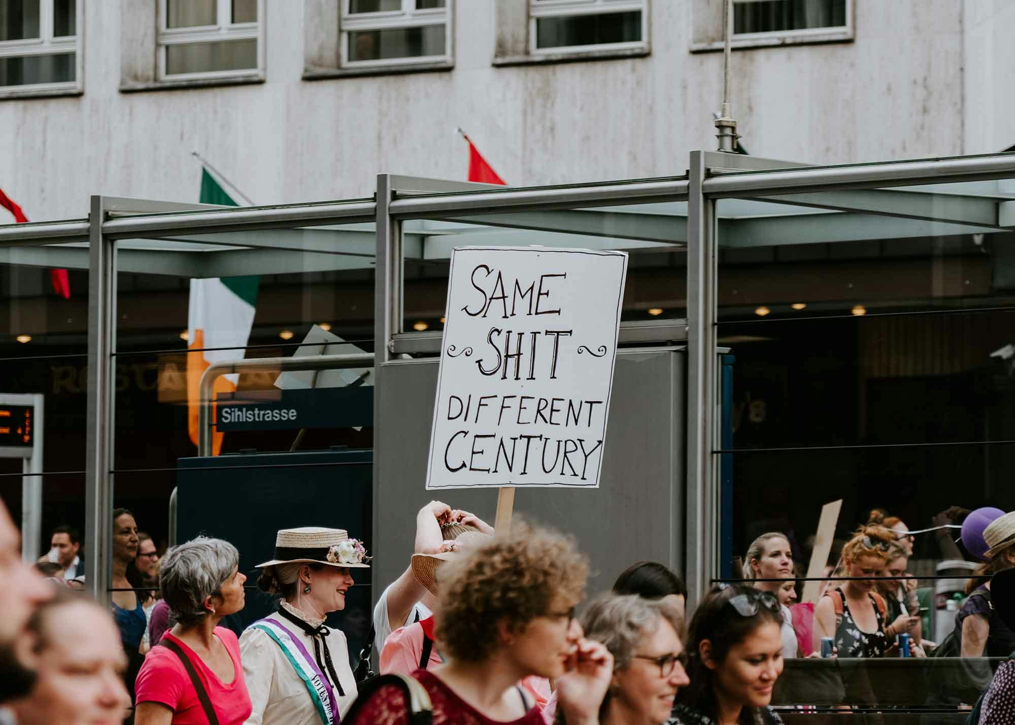 Protester reading a sign that says "same shit different century"