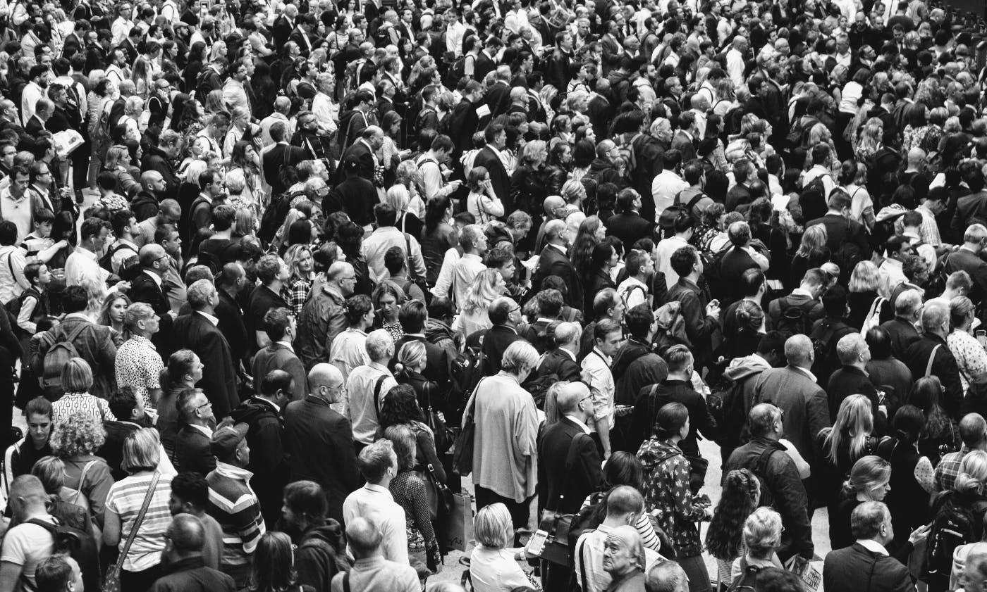 a black and white photo of a mass of people all facing and moving in the same direction