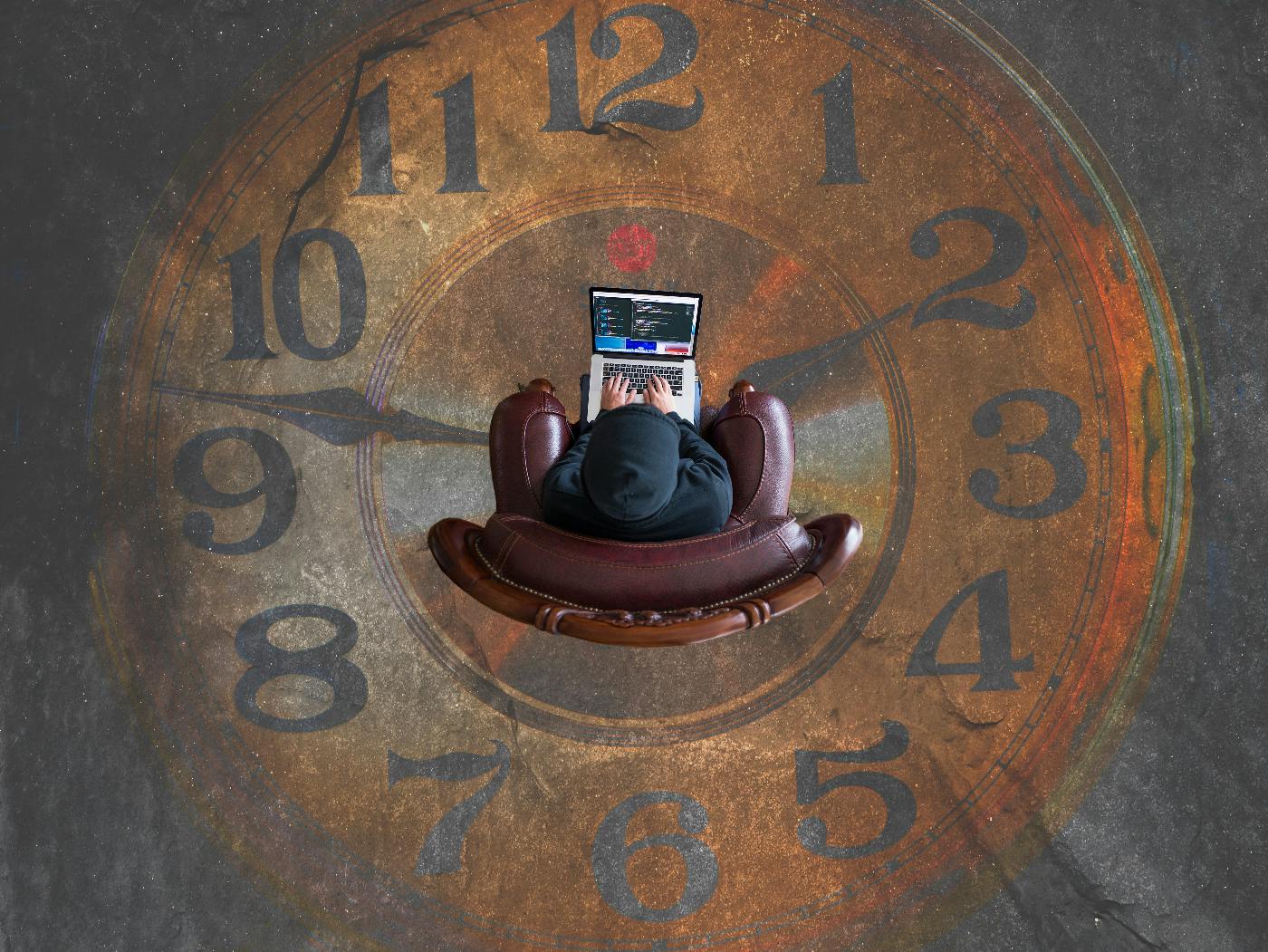 An overheard view of a person in a hoodie sitting in a leather chair on a floor that is painted like a clock face