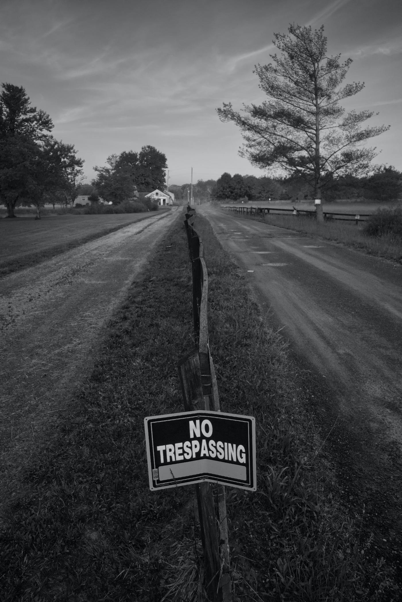 Empty road with a fence in the middle and a no trespassing sign.