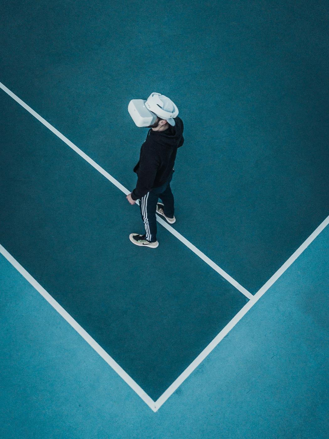 A man in a black sweat suit standing on a tennis court wearing a VR headset
