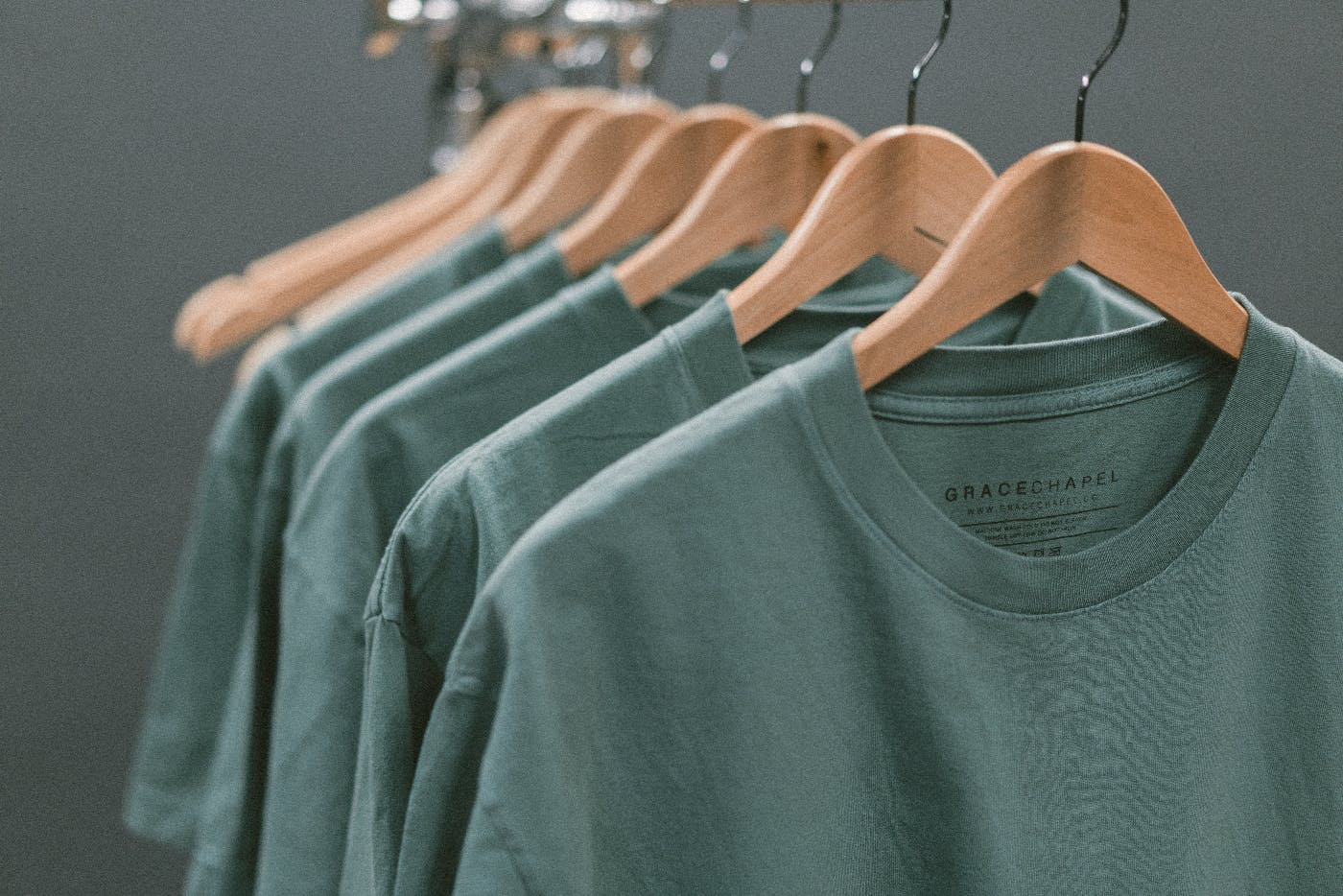 A rack with green T-shirts on wood hangers