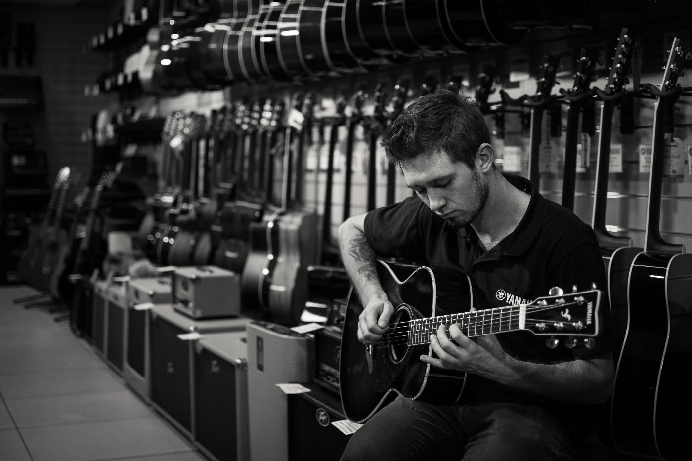 A guy playing an acoustic guitar in front of a wall of guitars