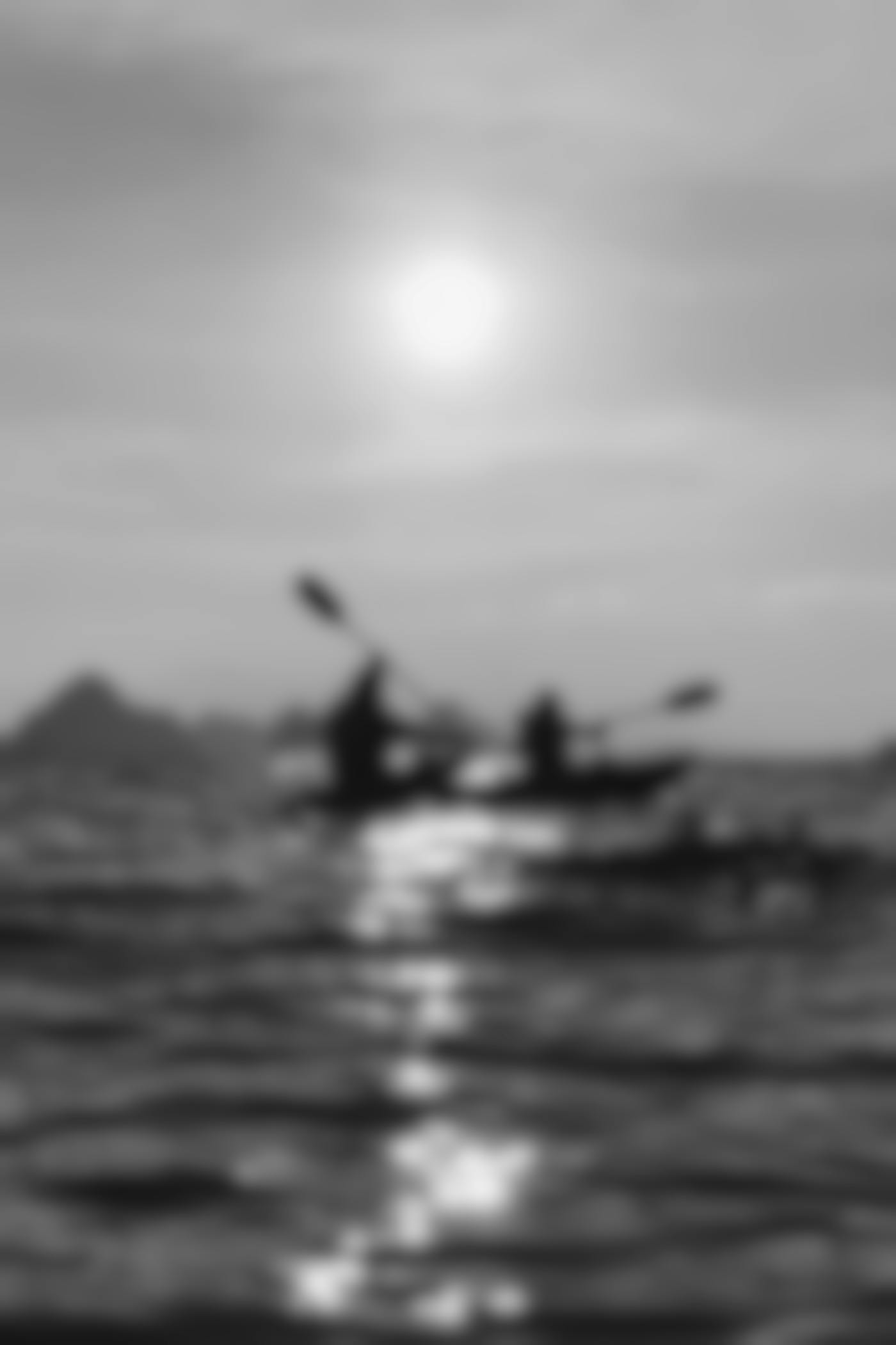 Silhouette of two people in kayaks paddling across a lake