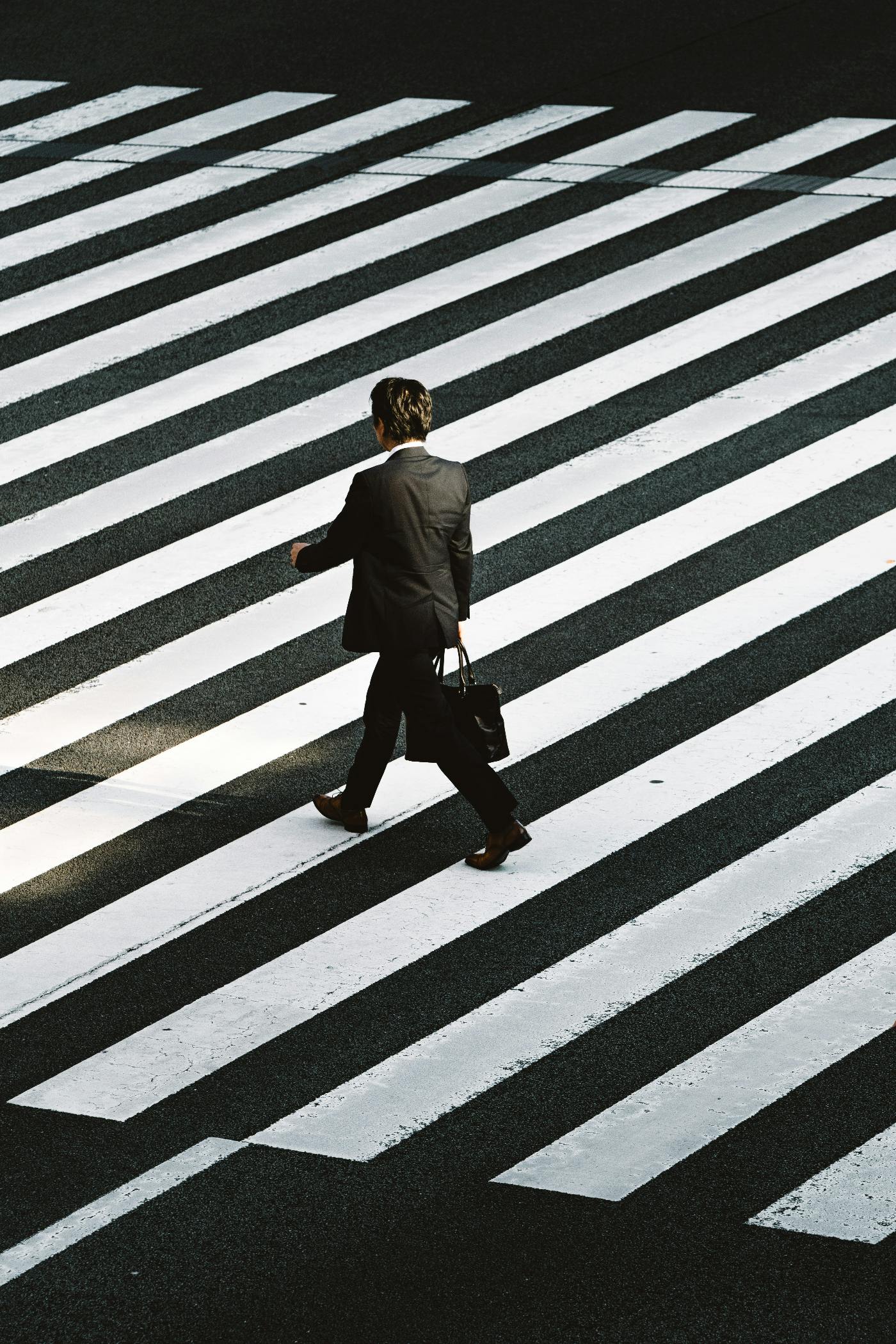 A man in a suit with a briefcase crossing a black and white crosswalk.