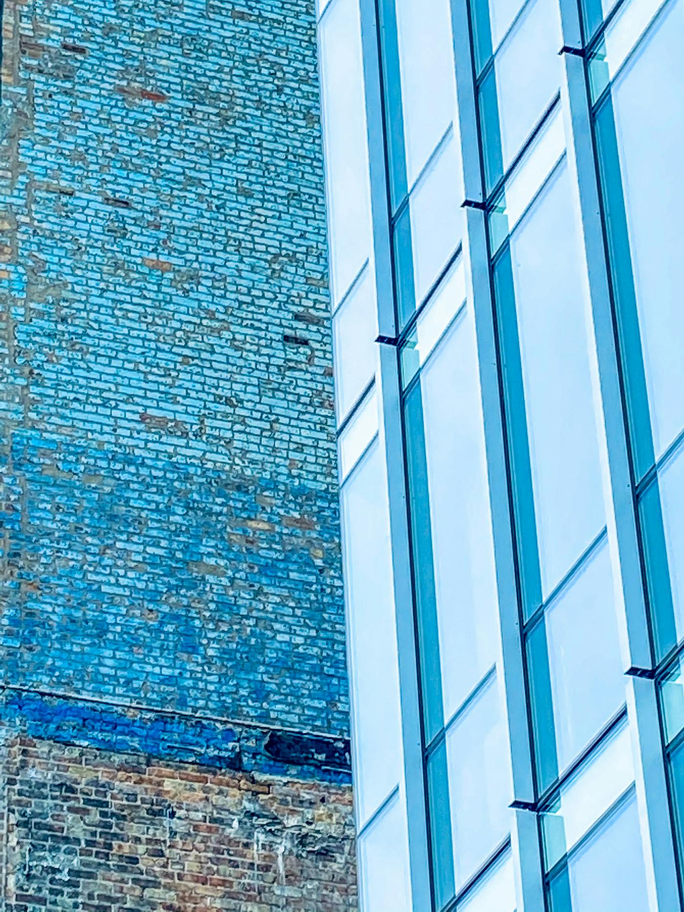 Two buildings at right angles, one brick paitned blue the other modern steel and glass reflecting blue