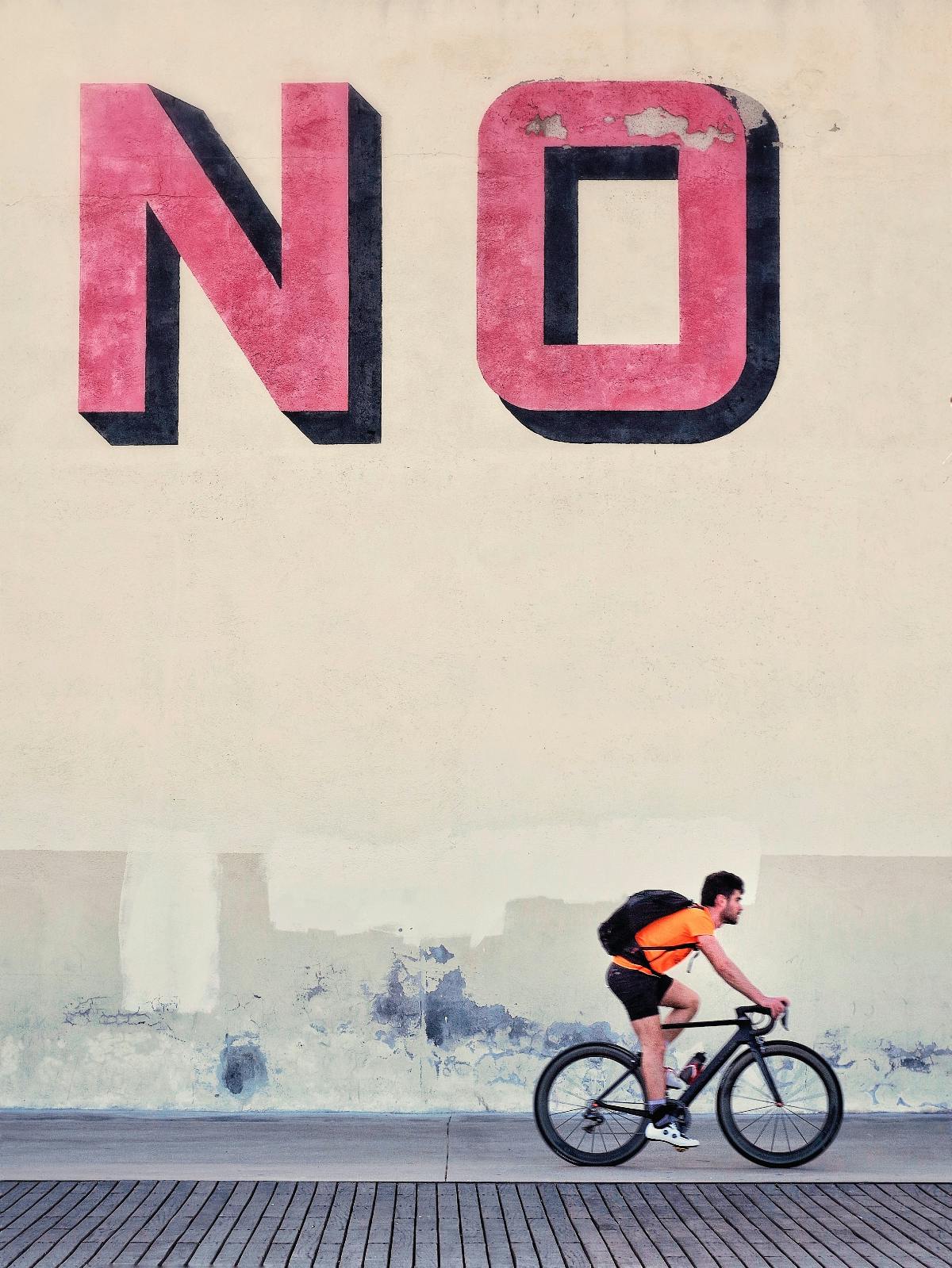 a guy on a bike riding past a wall where someone has painted the word NO