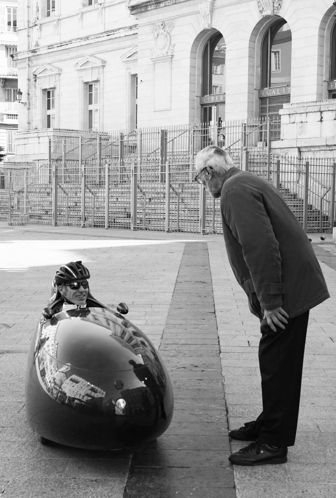 An older man speaking to a younger man in a small, one person vehicle.