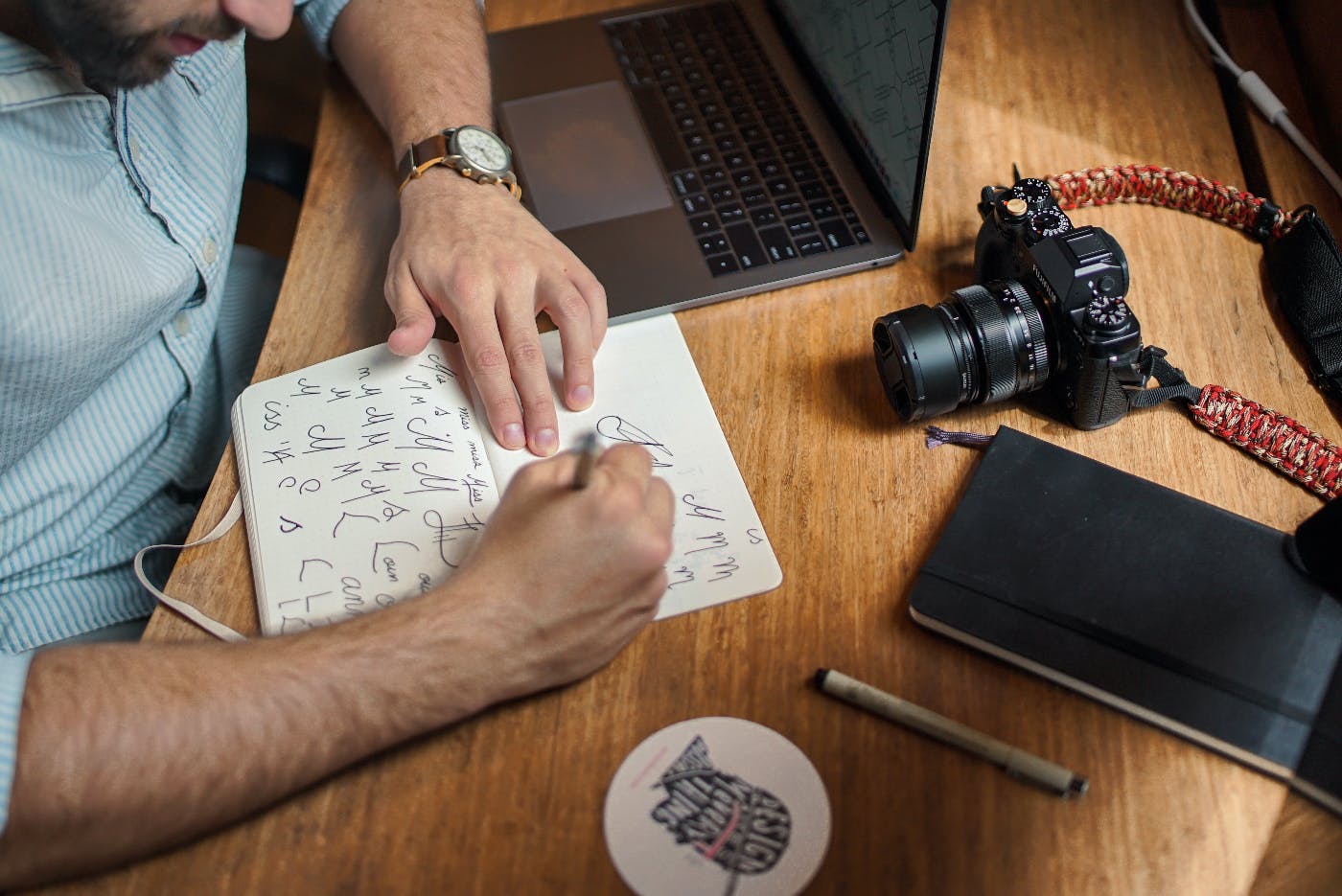 A guy sitting at a table with a camera, Moleskine, pen and he's working on a logo in a notebook
