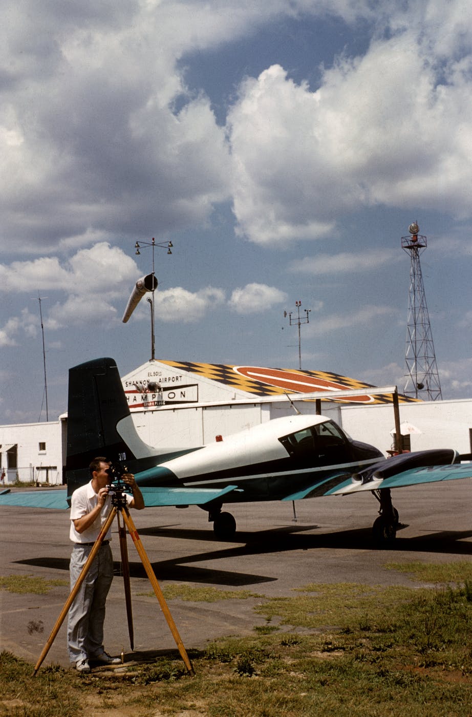 A man looking through a transit, standing in front of a white and blue plane