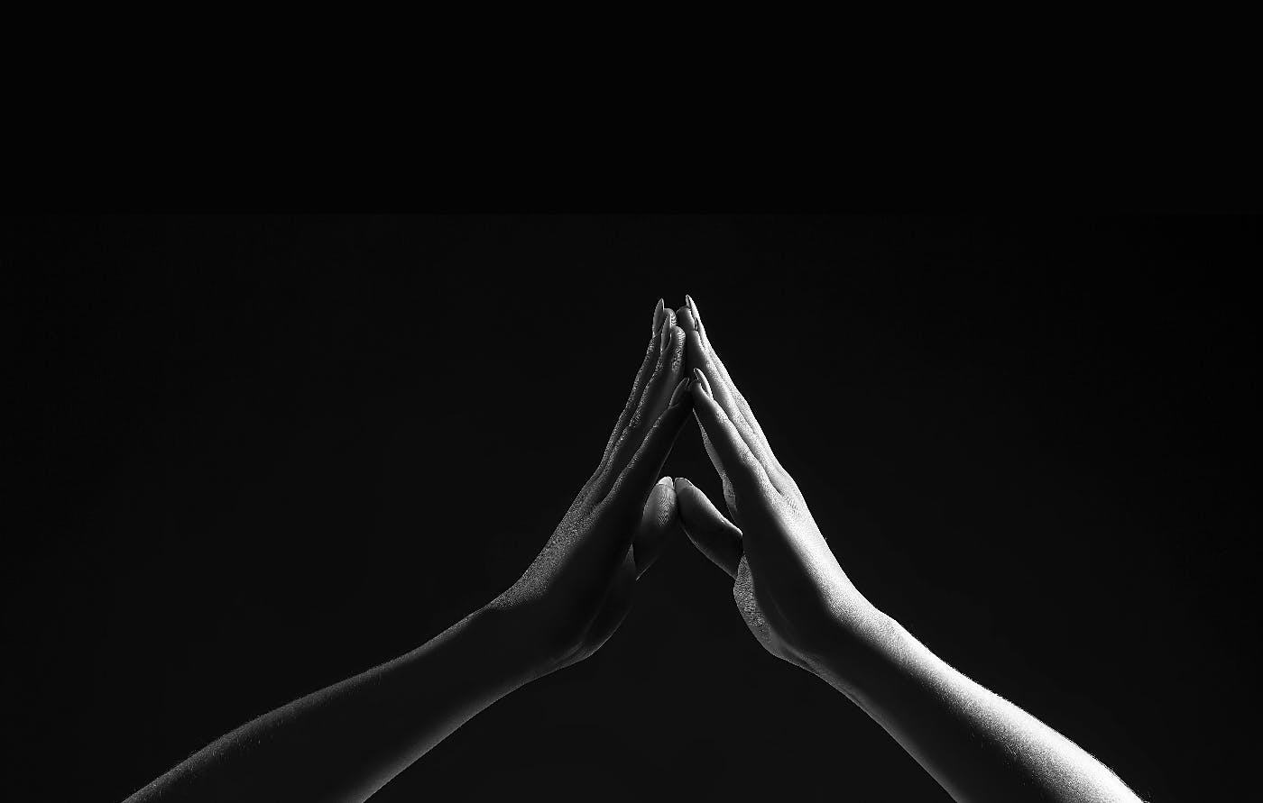 A grey scale image of two women's hands touching in darkness