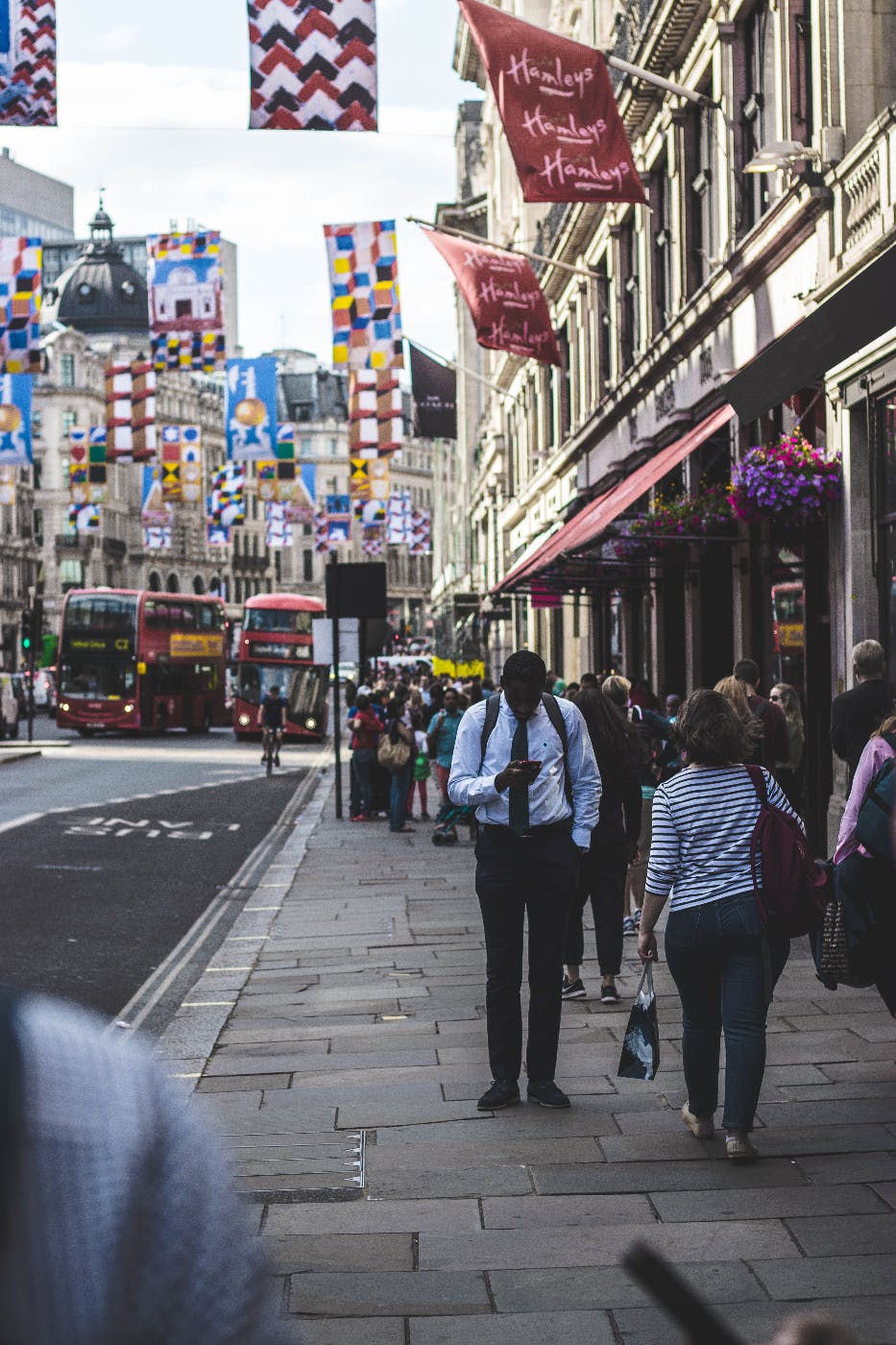 A man standing still on a crowded, busy sidewalk, looking at his smartphone