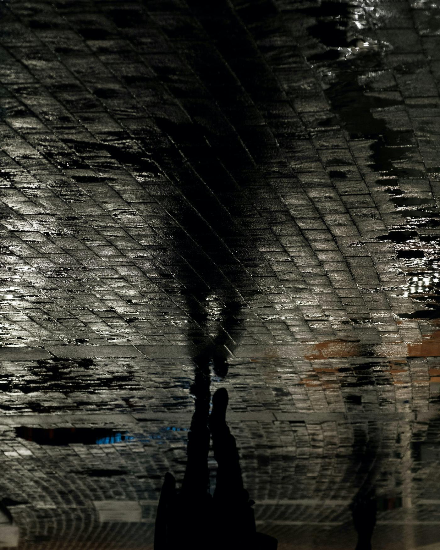 A man walking down a wet street his reflection in the wet stones makes him appear upside down