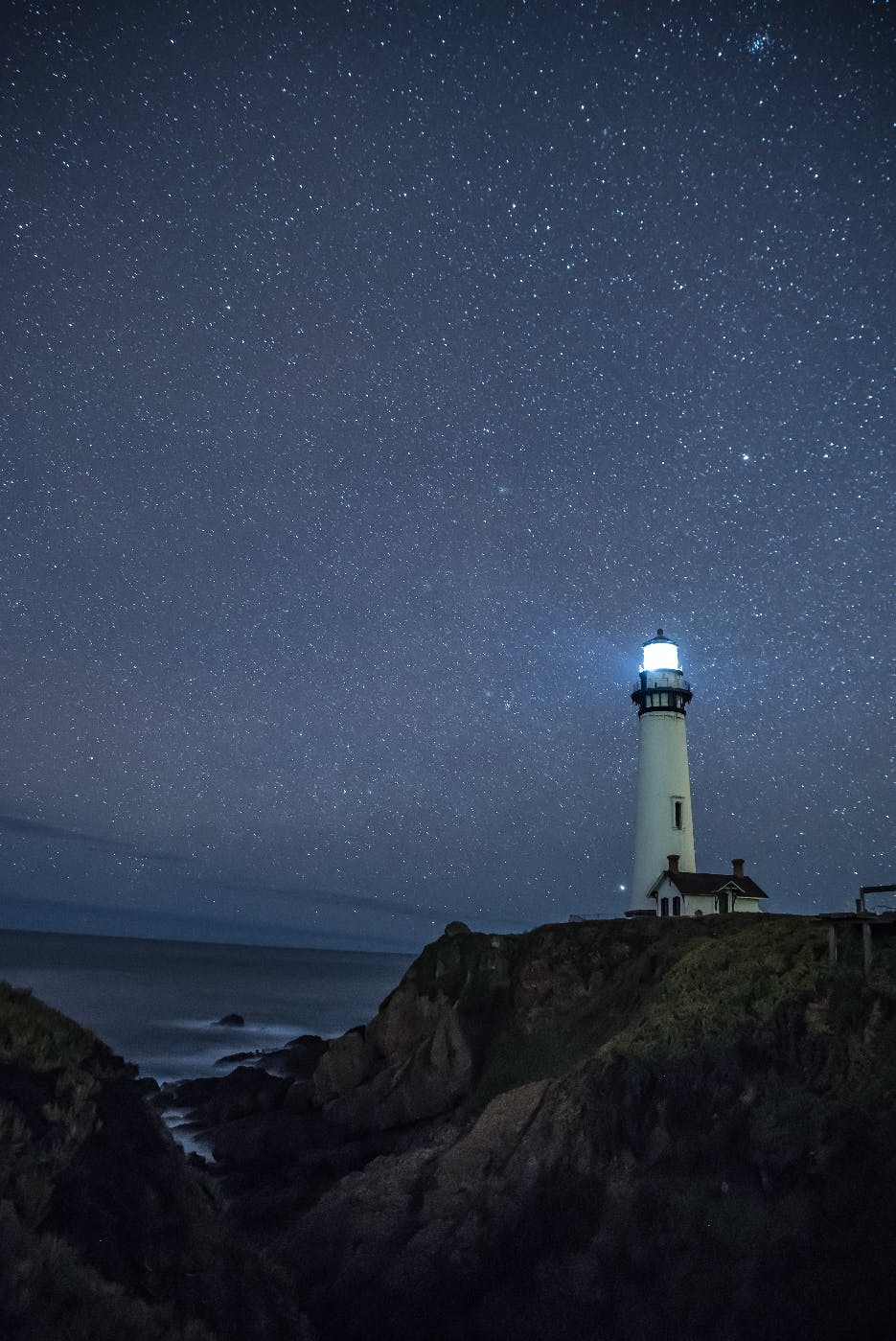 a lighthouse on a rocky cliff against a star filled sky