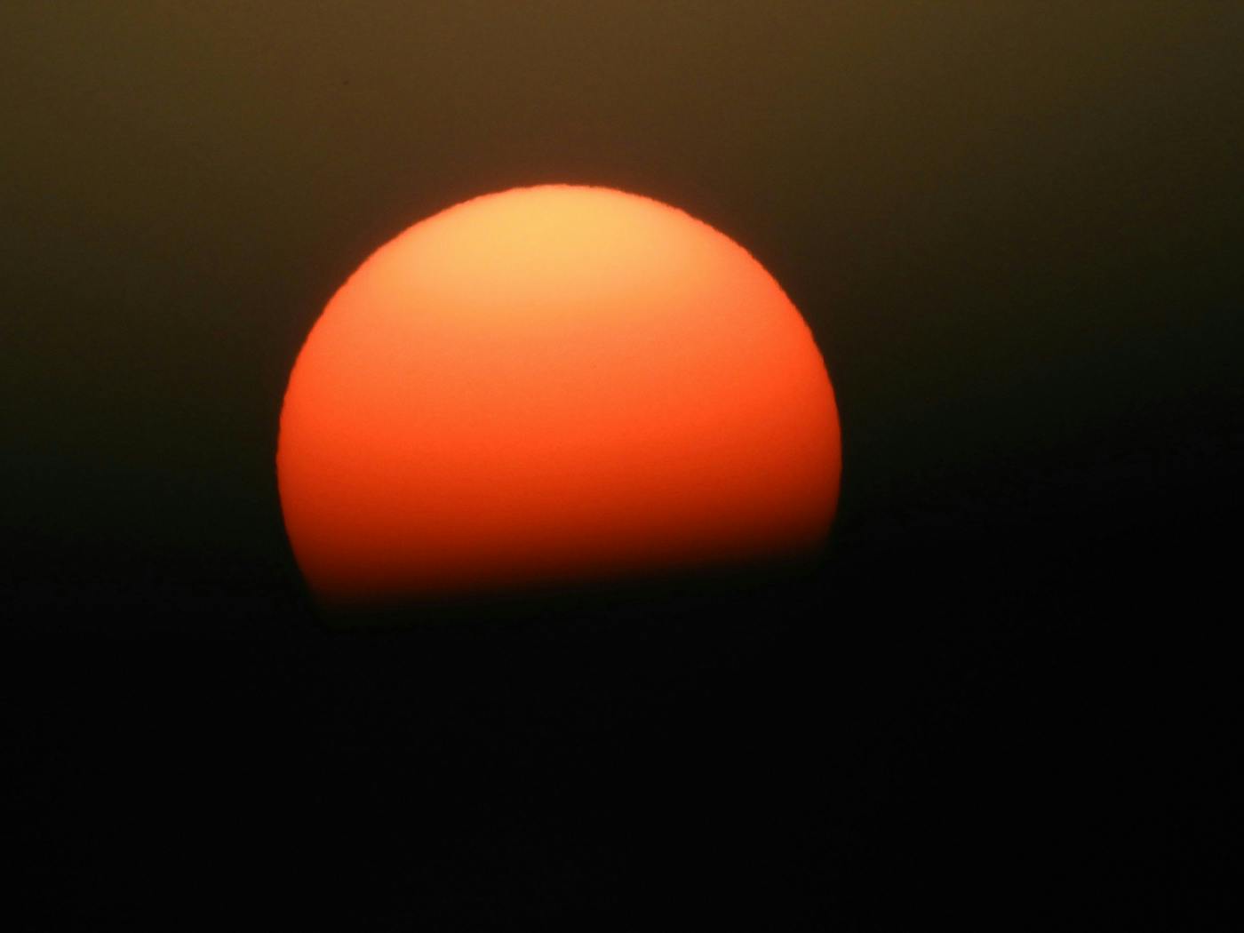 a sunset, the sun looking like an orange ball slipping into black ink