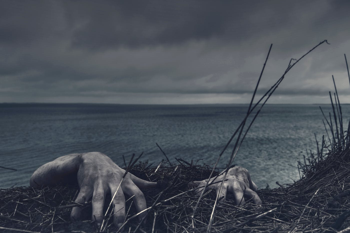 A cliff overlooking the ocean with two pale ghostly hands coming over the edge.