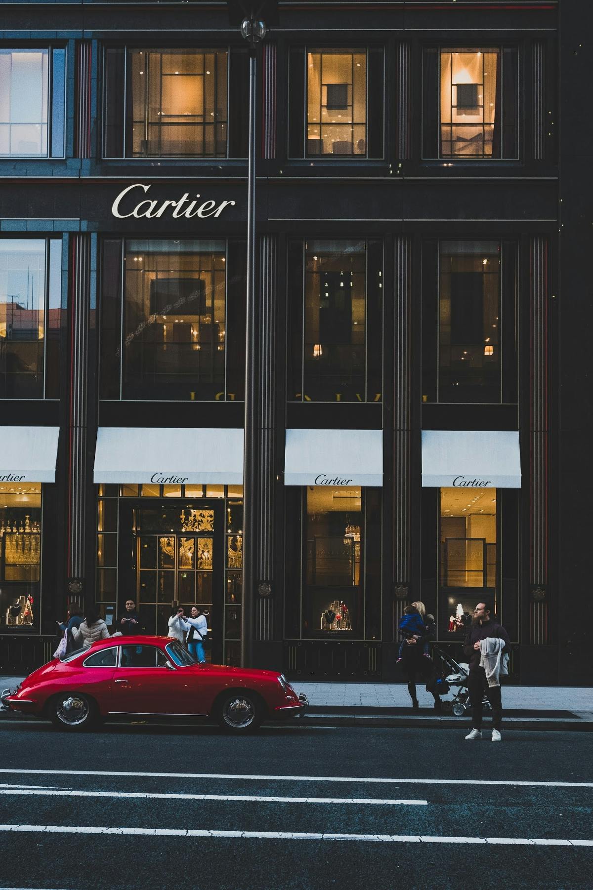  A red foreign car parked in front of the Cartier buildiing.