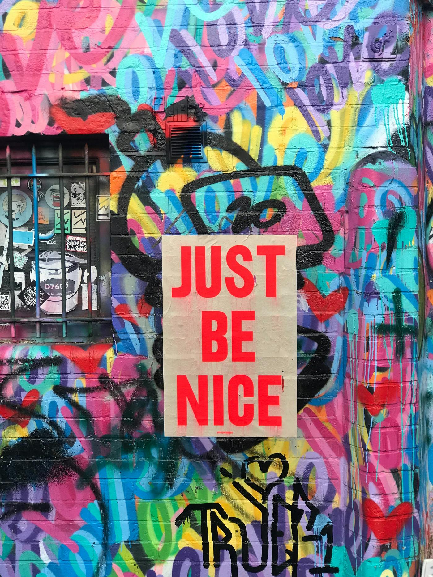 A multi-colored wall with the words Just Be Nice in the middle.