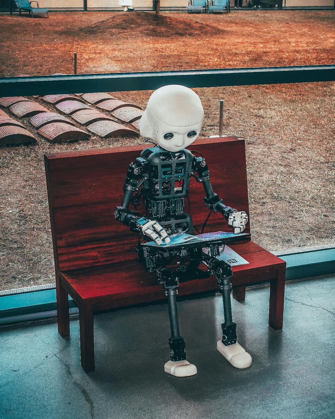 A little boy robot sitting on a bench playing a game