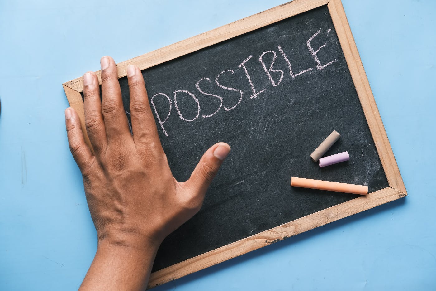 A small chalk board with the word impossible written on it and a man's hand covering the I and M