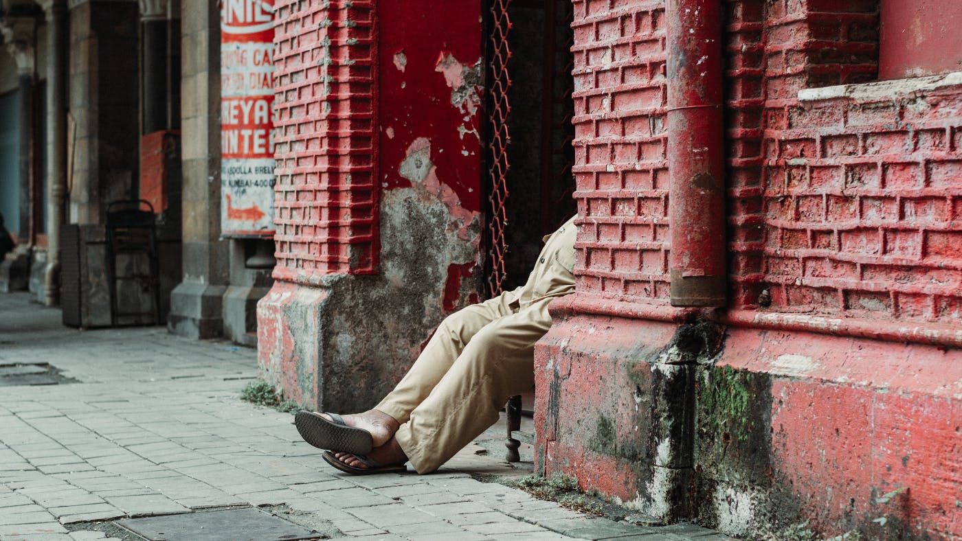 An older gent sitting on a chair in a doorway on a dirty street