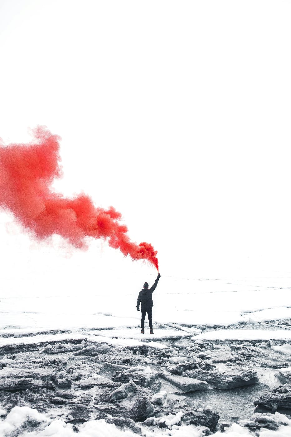 A person standing on a white frozen landscape, releasing red smoke