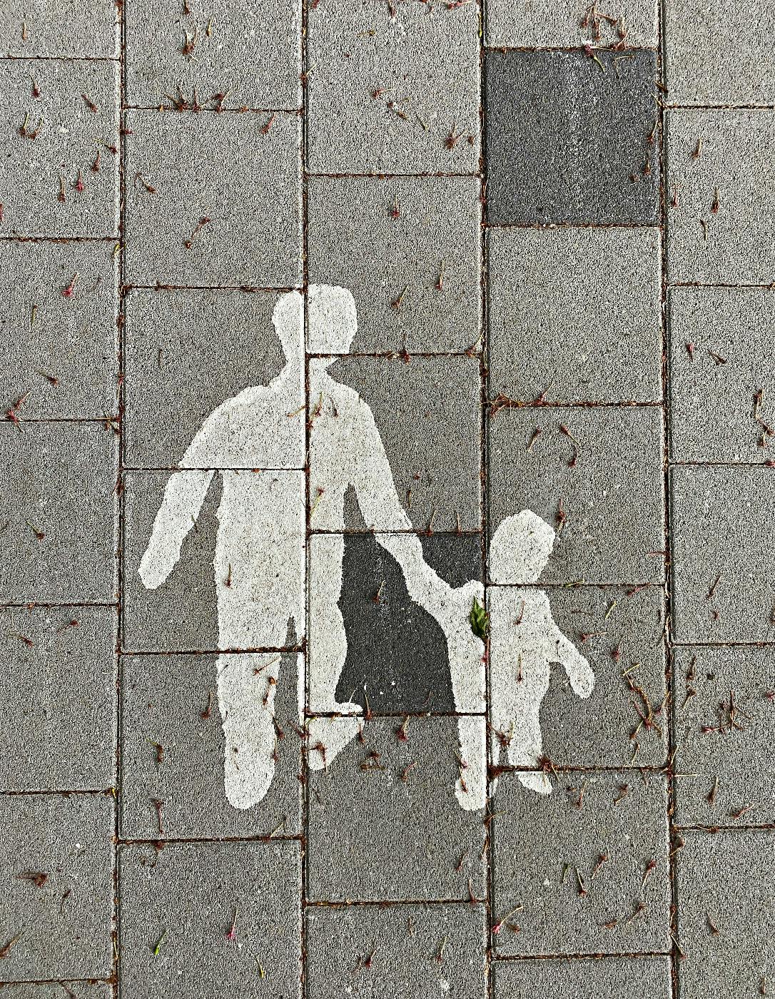 A painting in the sidewalk, outline of an adult holding  a child's hand