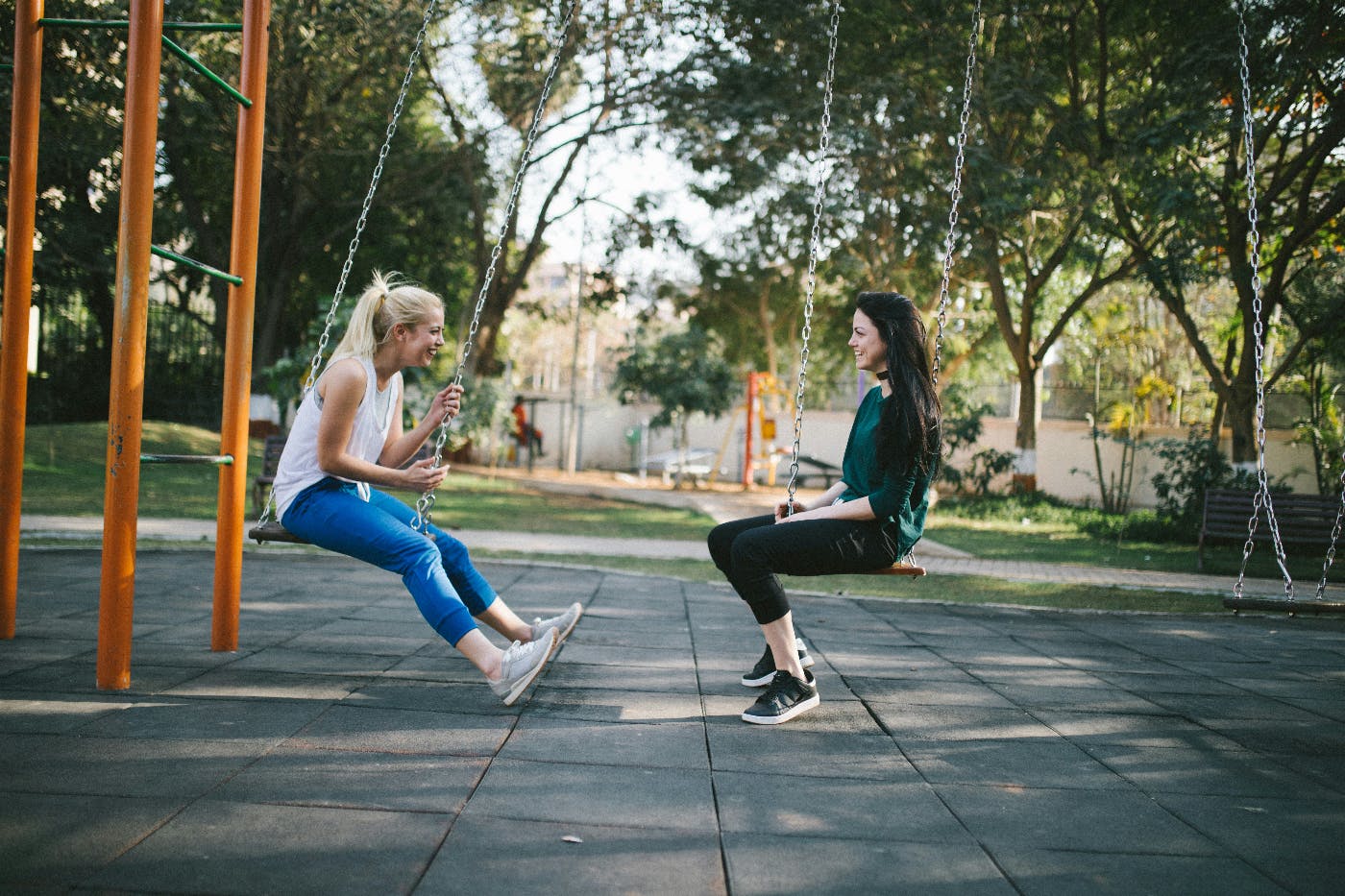 Two women on a swing set talking to each other