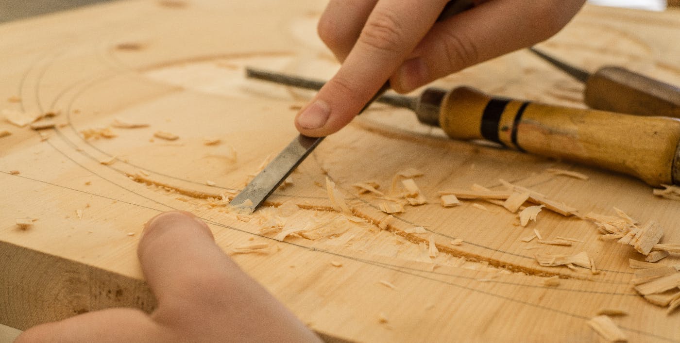 two hands using a slim chisel to carve a design in a blocck of wood