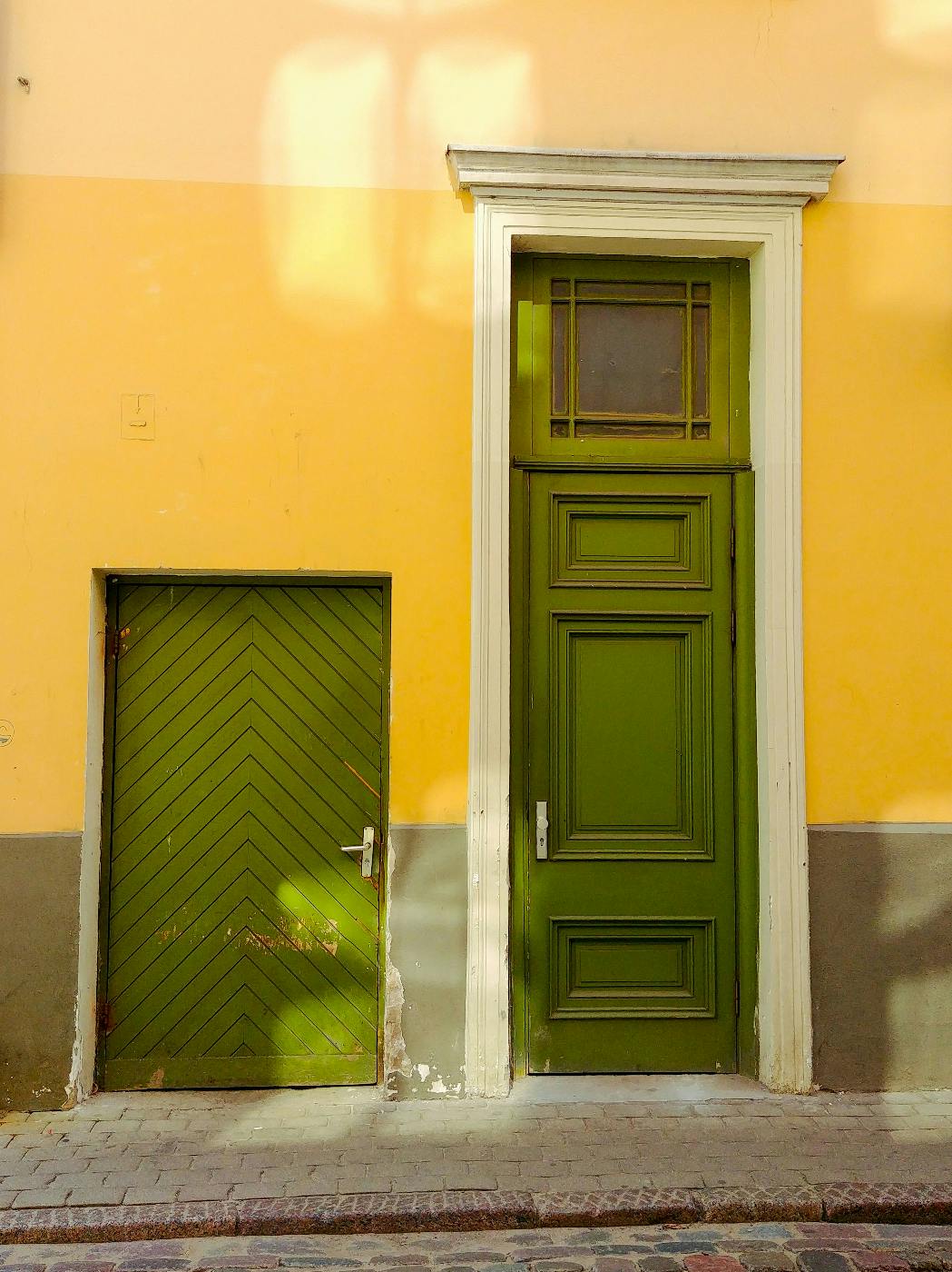 Short and tall green doors in a yellow wall