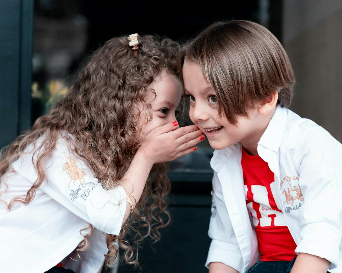 A little girl whispering to a little boy