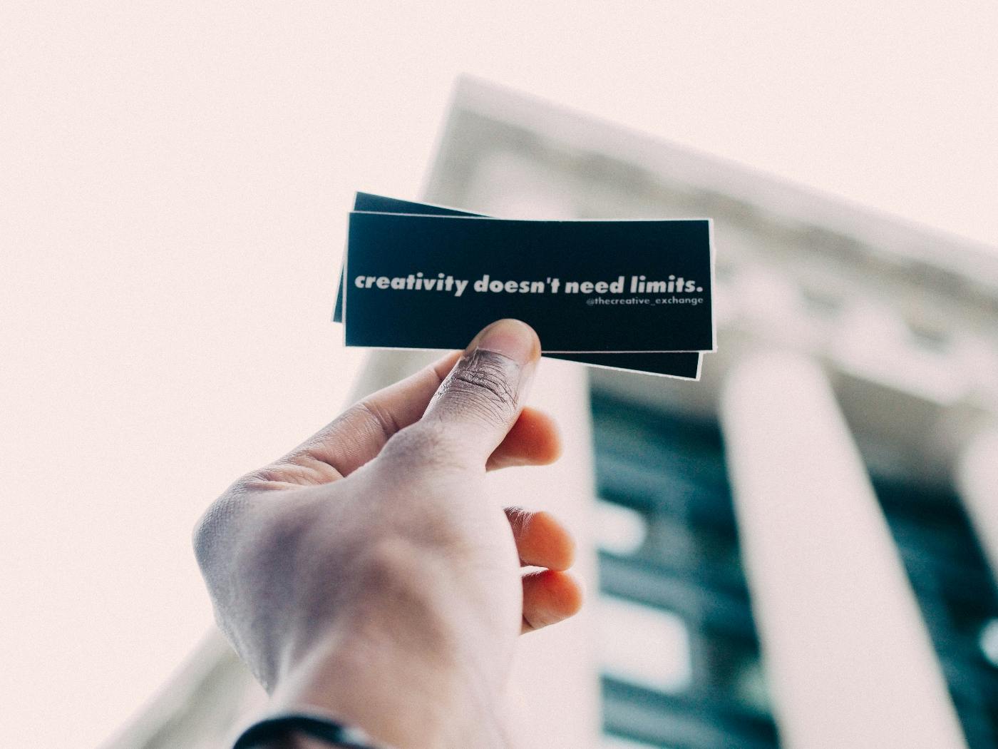 A hand holding a rectangular black card that reads: creativity doesn't need limits
