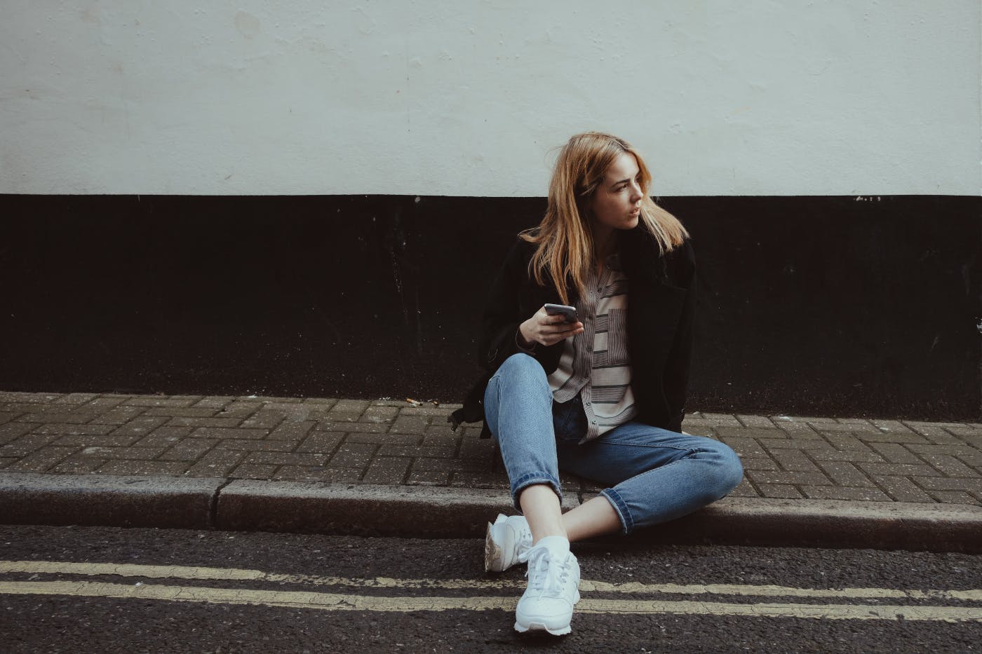 A girl with her cellphone sitting on a brick sidewalk